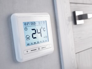 Digitales Raumthermostat zeigt 24 °C an und ist an einer Wand neben einer Tür montiert.