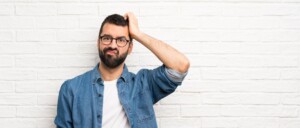 Ein Mann mit Brille kratzt sich nachdenklich am Kopf und blickt fragend zur Kamera.