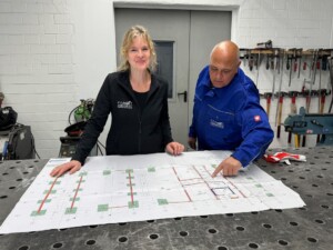 Zwei Mitarbeitende der ASRODENT GmbH besprechen gemeinsam einen technischen Plan an einem Werkstatttisch.