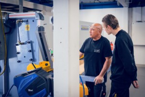 Mitarbeiter erklärt die Bedienung der Maschine für Metallarbeiten.