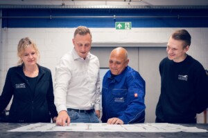 Teambesprechung in der Werkstatt mit Konstruktionsplan auf dem Werktisch.