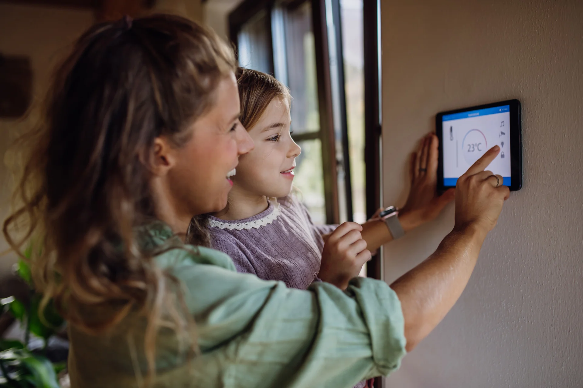 Erwachsene und Kind bedienen gemeinsam ein Smart-Home-Tablet zur Temperatursteuerung.