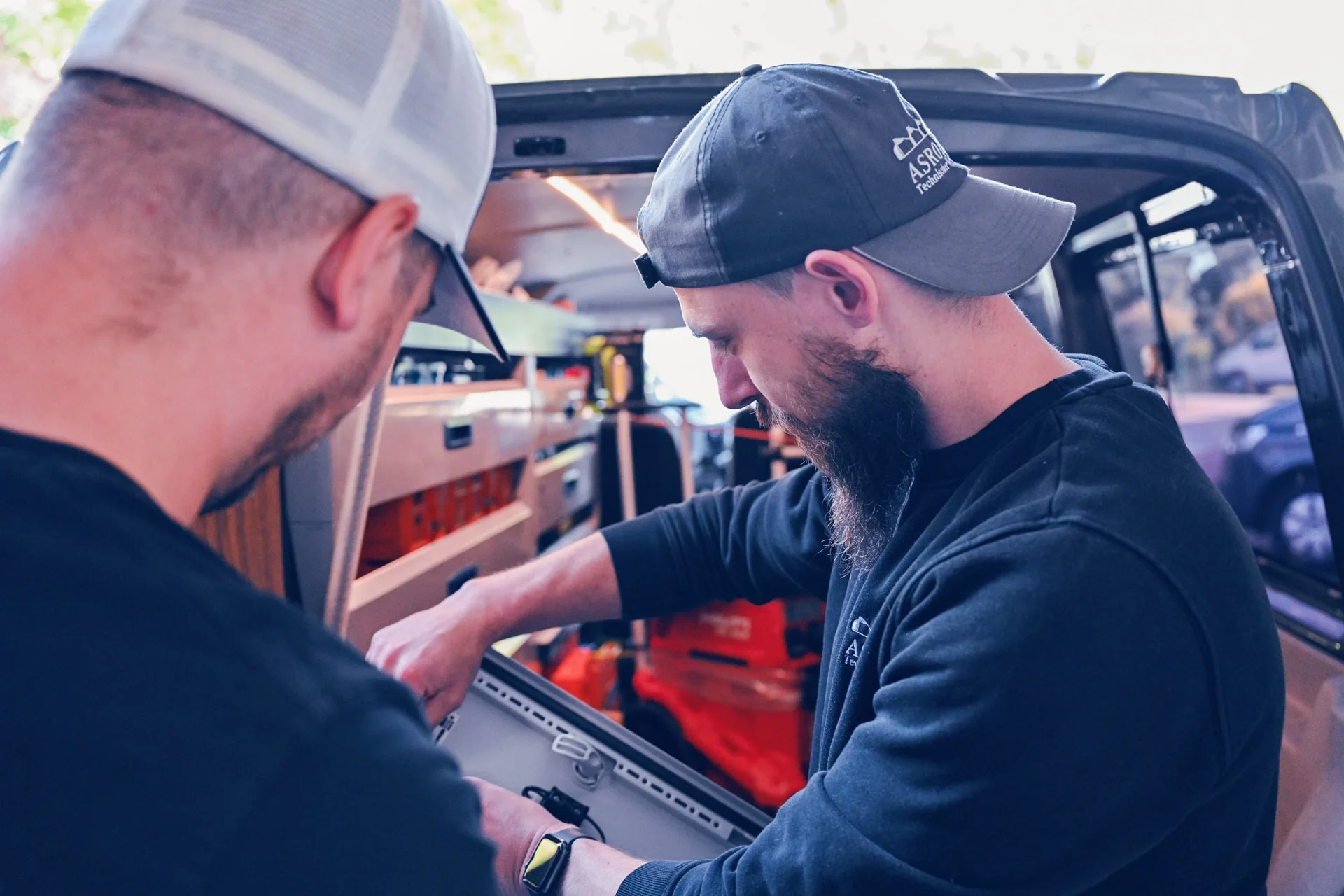 Zwei Mitarbeiter reparieren einen Schaltkasten. Im Hintergrund ist der Firmentransporter mit Werkzeug.